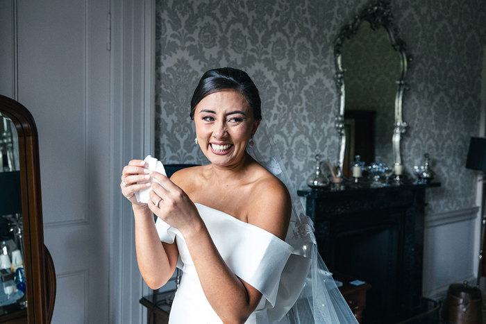 A Bride Wearing An Off Shoulder Wedding Dress Looking Emotional While Holding A Handkerchief