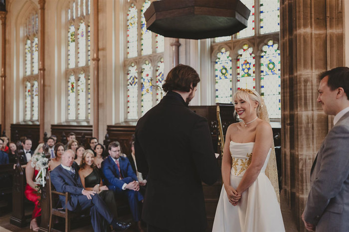 a bride and groom standing in front of guests in a church with stained glass windows.