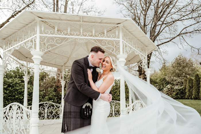 a bride and groom embrace with the bride's veil floating behind her