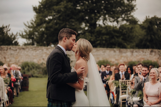 A Bride And Groom Kissing As Guests Looks On