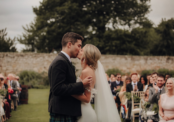 A Bride And Groom Kissing As Guests Looks On