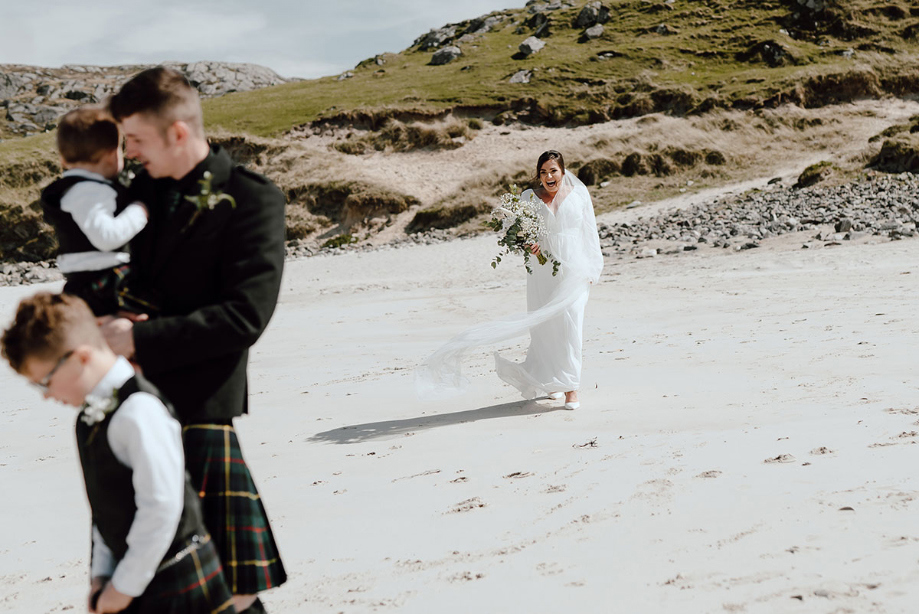 Bride walks towards groom and children for first look on beach