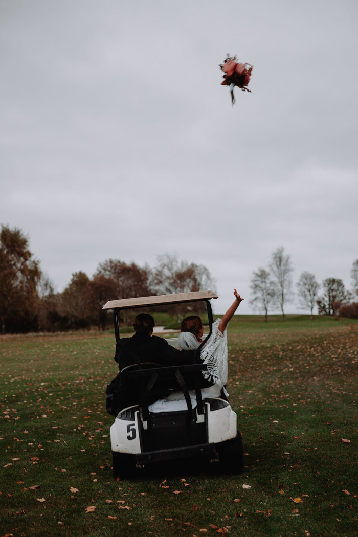 bride and groom drive away in golf buggy with bridal bouquet thrown up in the air as they go