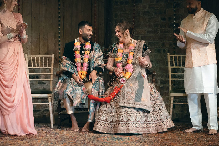 A bride and groom wearing indian attire sitting on chairs.