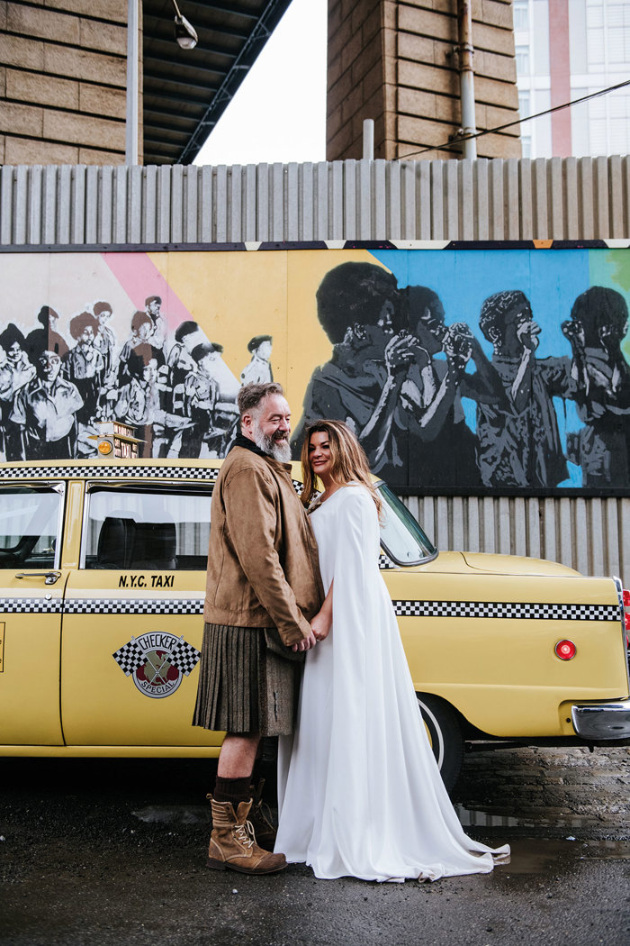 A person and person holding hands in front of a yellow New York taxi cab