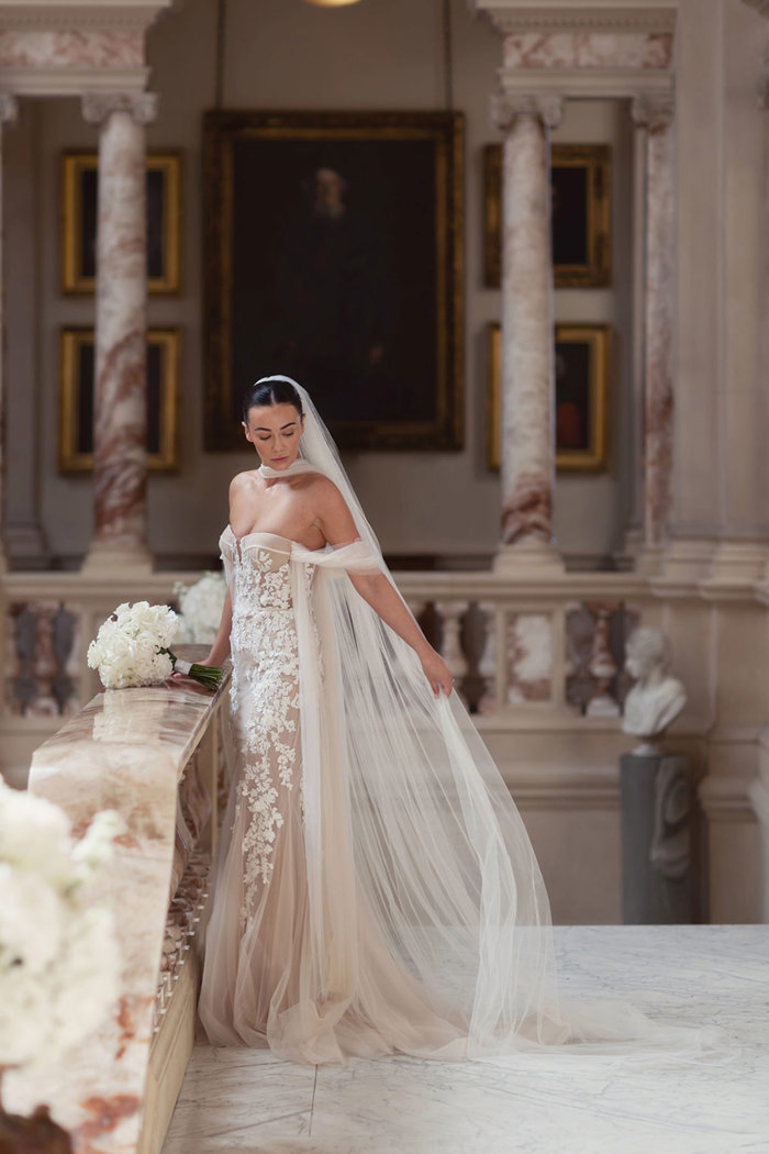 A bride in a Berta Privee wedding dress from Opus Couture on a marble staircase.