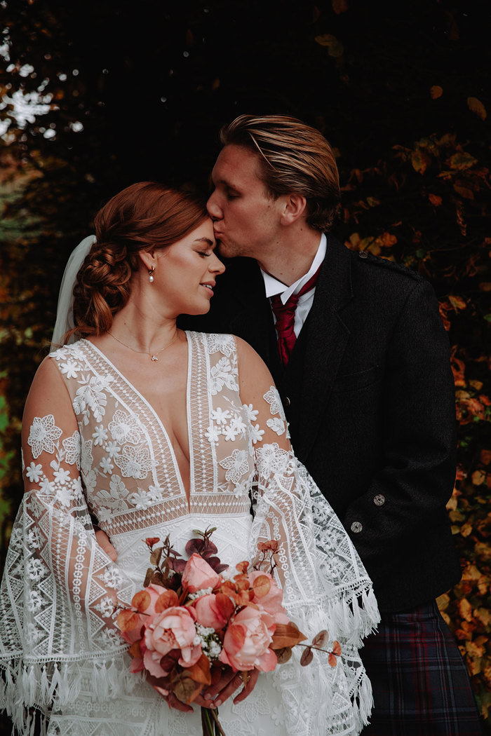 blonde groom kisses brunette bride on forehead, as they both lean their upper bodies in towards each other