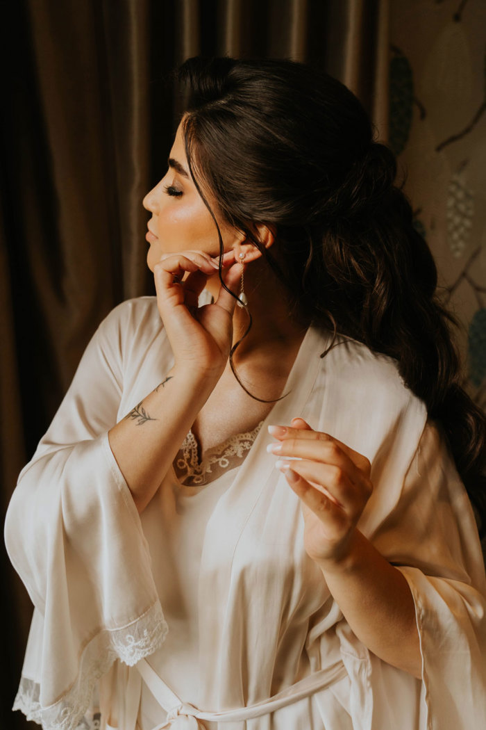 A woman in a white silk robe putting in earrings