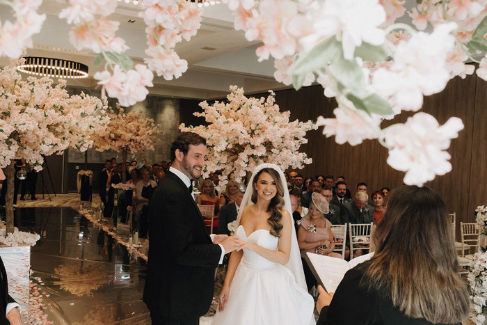 a bride and groom look towards a celebrant during a wedding ceremony at Cameron House. There is lots of cherry blossom decor.