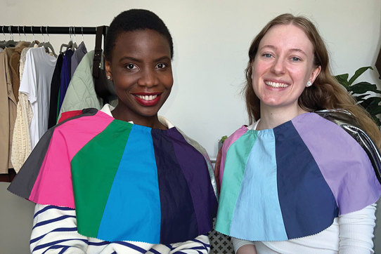 two women sit side by side with differently coloured fabric draped across their shoulders for comparison 