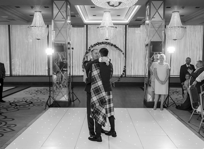 two grooms hugging while doing a first dance on a light-up dance floor