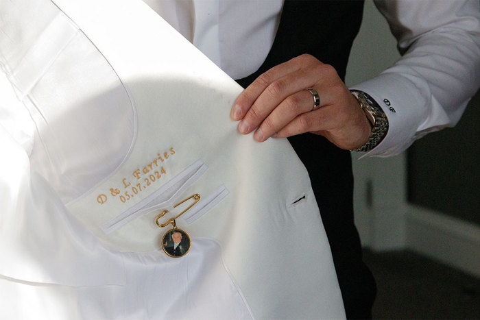 The inside of a white suit jacket with gold embroidery that reads 'D & L Farries 05.07.2024' 