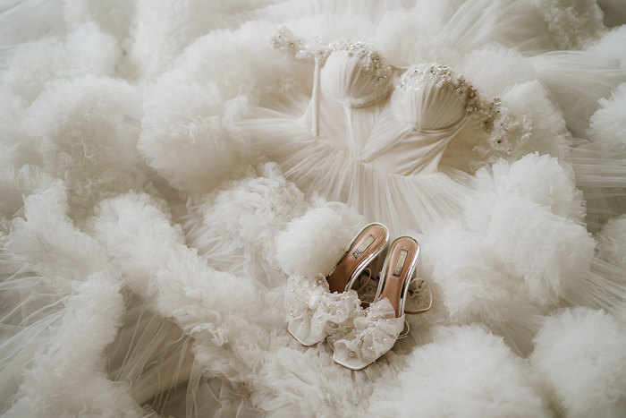 A wedding dress with a voluminous tulle skirt with a pair of white high heels lying on top of it