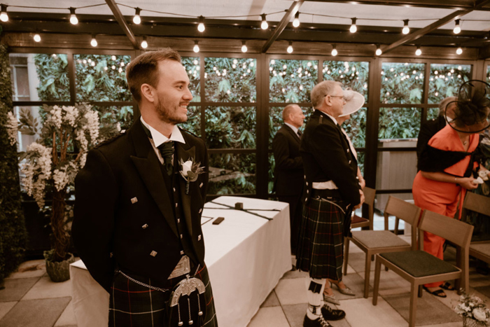 Groom smiles as he waits for bride at the top of the aisle