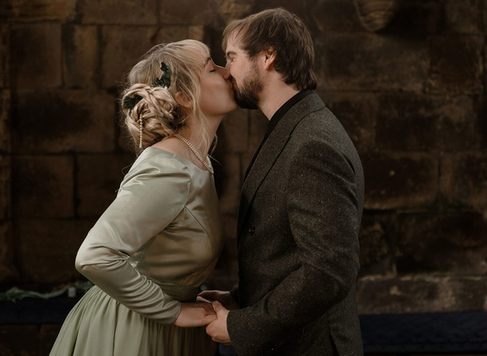 a bride wearing a pale green dress and groom wearing a dark tweed suit kissing