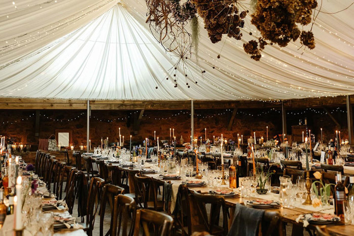 a draped ceiling space with rows of long wooden dining tables decked out with tall candlesticks and place settings