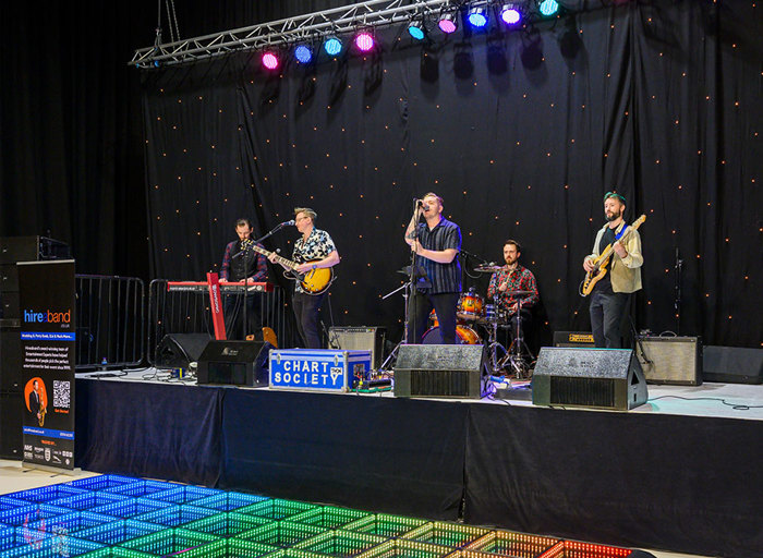 A band performs on a stage in front of a light up dance floor 