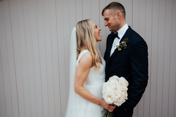 Bride and groom smiling at each other with rose bouquet