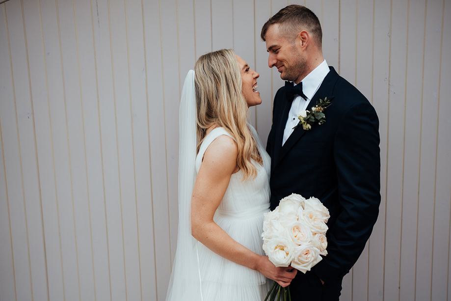 Bride and groom smiling at each other with rose bouquet