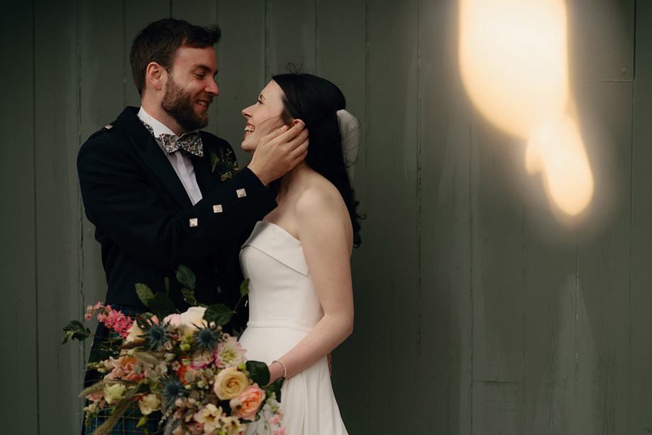 Groom caressing brides face with pink and cream bouquet