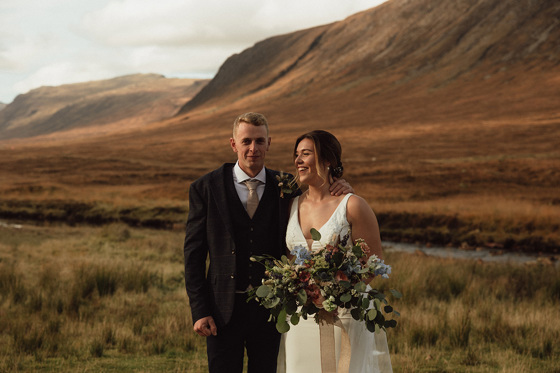 Bride holding bouquet with her groom with hills beyond