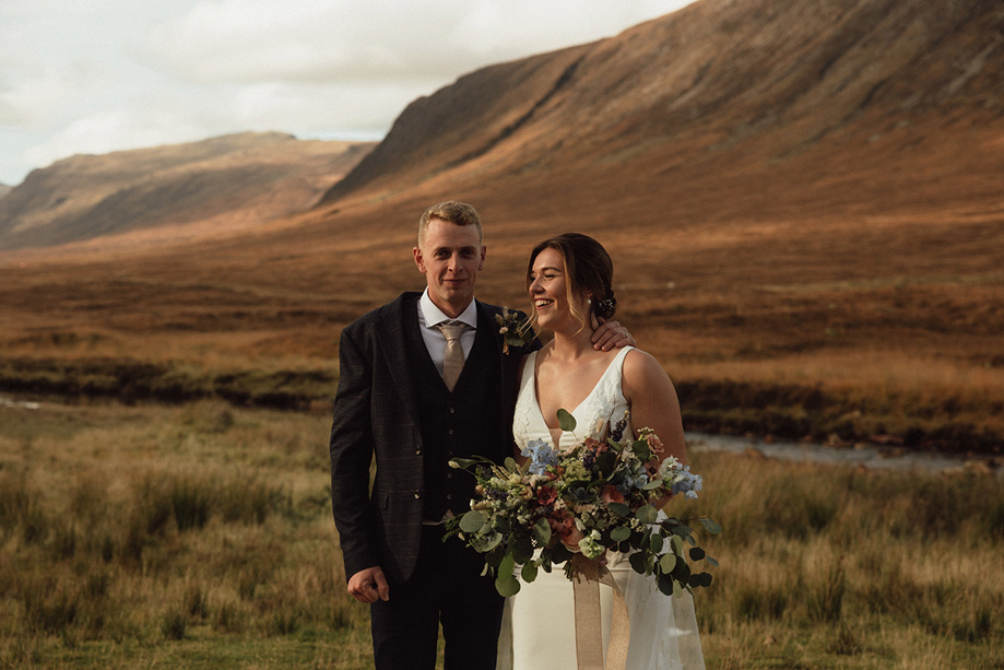 Bride holding bouquet with her groom with hills beyond