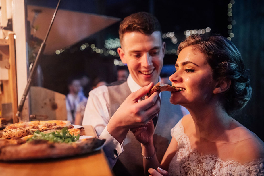 Groom feeds slice of pizza to his bride