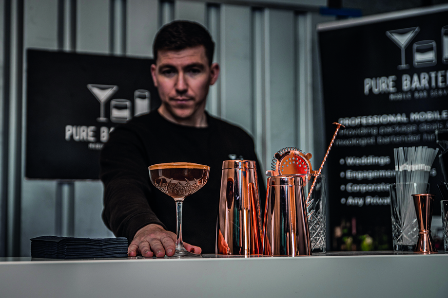 Owner of Pure Bartending Michael Mckenzie behind the bar pushing cocktail to front