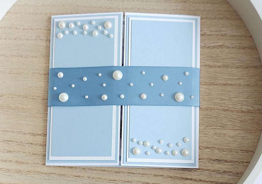 Blue invitation wrapped in blue ribbon, decorated with large and small pearls