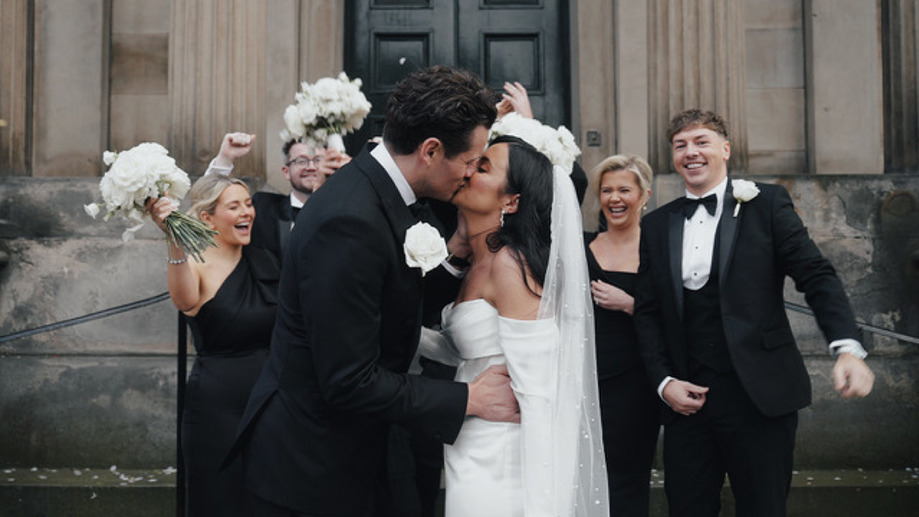 Bride and groom kiss with happy guests in background