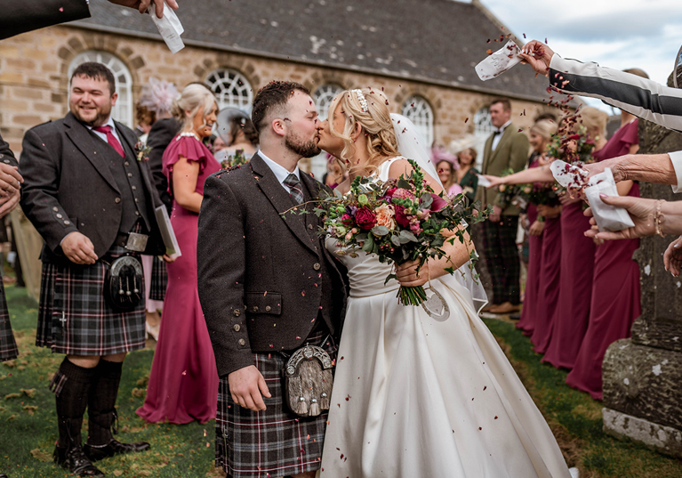 Bride and groom share a kiss during confetti shot by Magic Moments Studio
