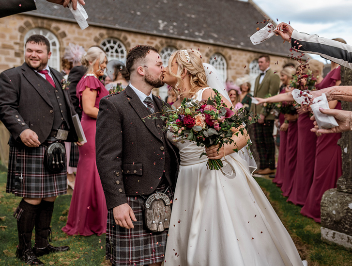 Bride and groom share a kiss during confetti shot by Magic Moments Studio