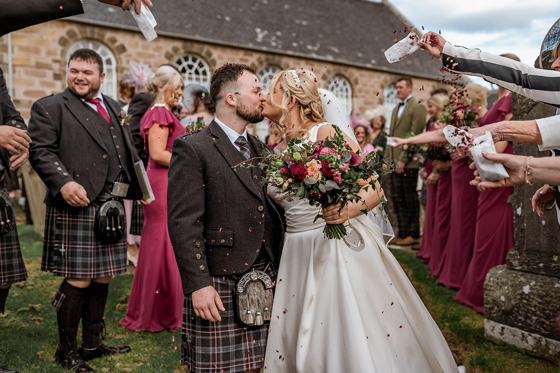 Bride and groom share a kiss during confetti shot by Magic Moments Studio