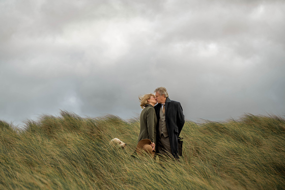 Couple share a kiss in long grass with their dog