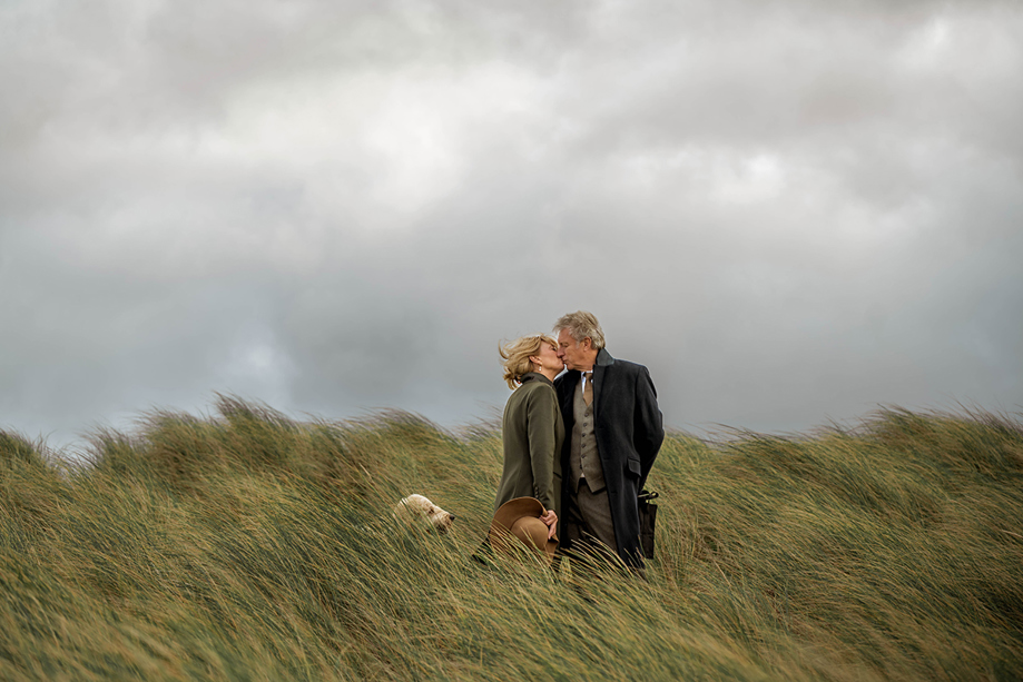 Couple share a kiss in long grass with their dog