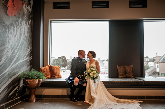 Bride and groom sitting in front of window smiling at each other