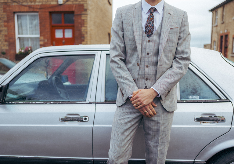 Body of man in three-piece suit standing in front of silver car