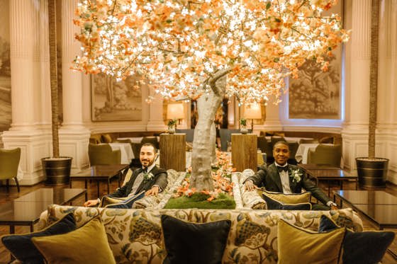 Grooms pose on seat with lit-up tree