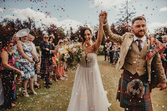 Bride and groom hold their hands up in air as they walk through confetti after getting married