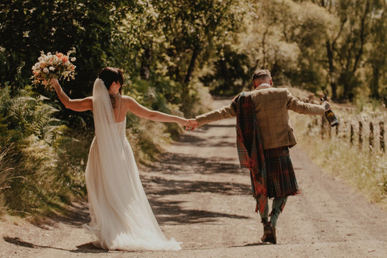 Bride and groom walking away with bouquet and bottle of champagne in hands