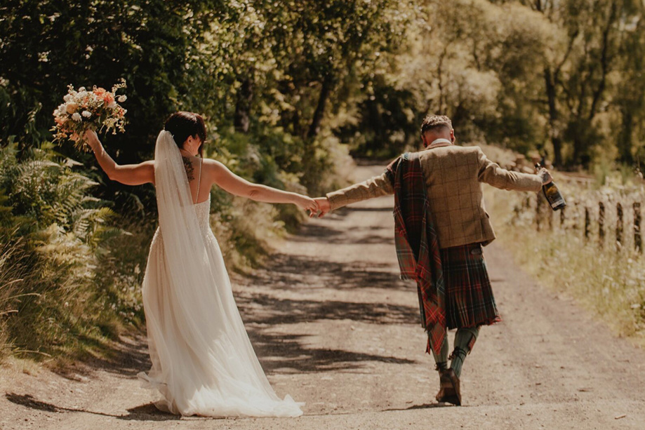 Bride and groom walking away with bouquet and bottle of champagne in hands