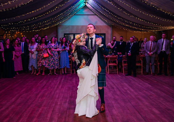 Bride wearing flower crown and leather jacket has first dance with her groom