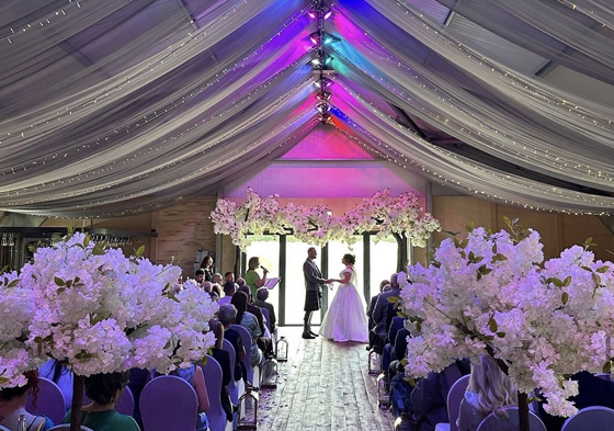 Bride and groom at the altar with draped, multicolour ceiling above them and flowers in foreground