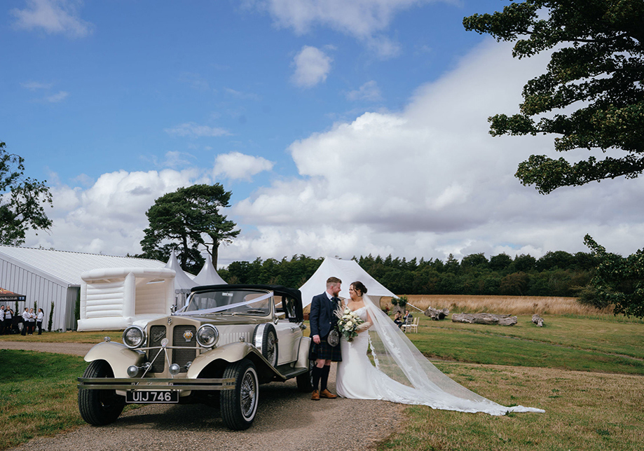 Bride and groom pose beside wedding car