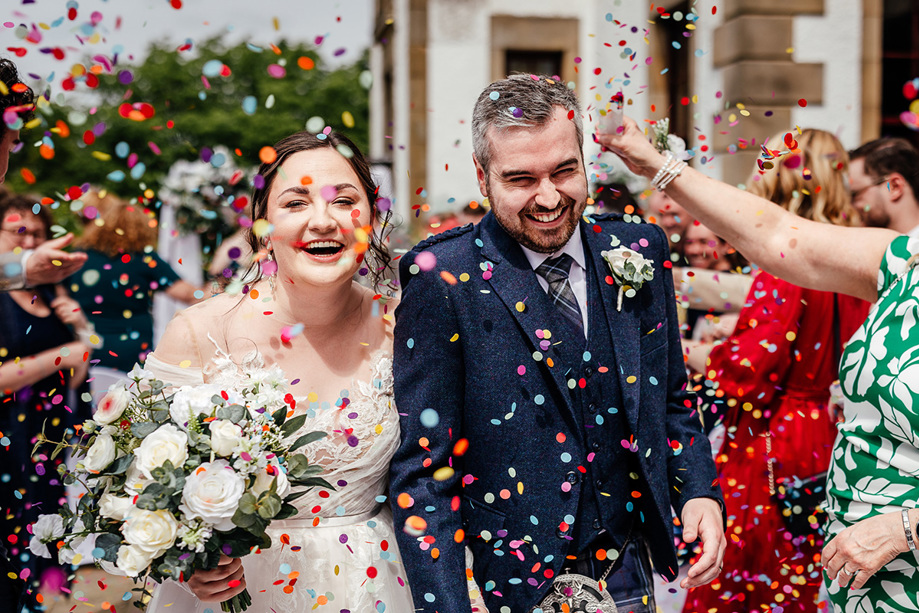 Bride and groom walk through rainbow coloured confetti