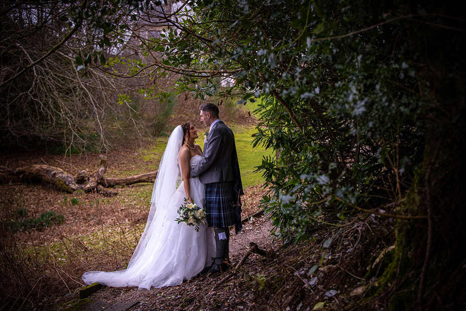 Bride and groom look into each others eyes amongst forest