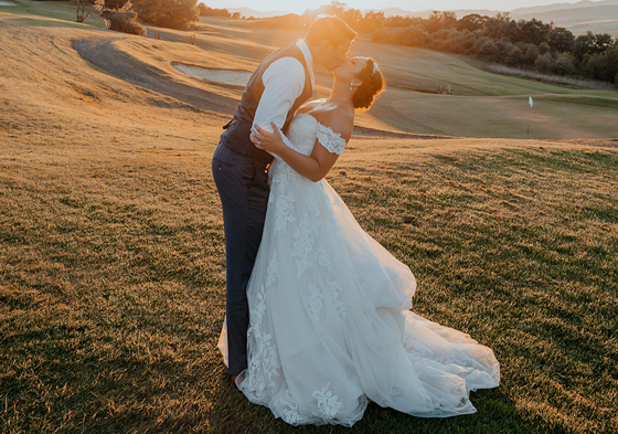 Bride and groom lean back to kiss at sunset on golf course