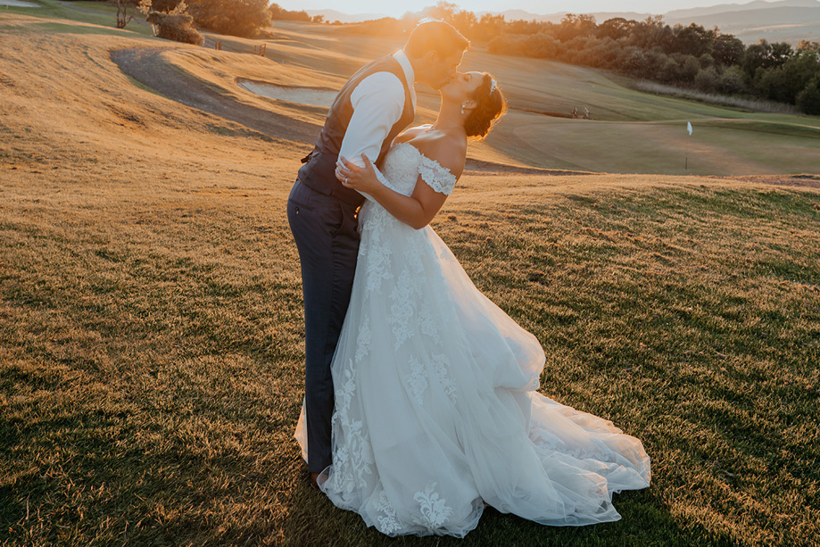 Bride and groom lean back to kiss at sunset on golf course