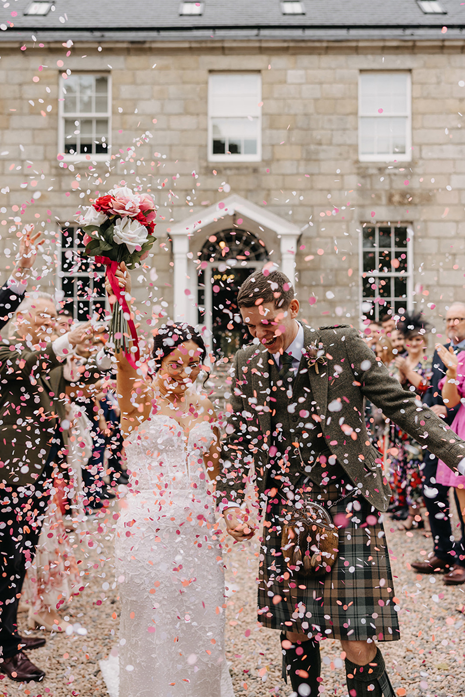 Bride and groom celebrate as they walk through confetti toss outside Elrick House.
