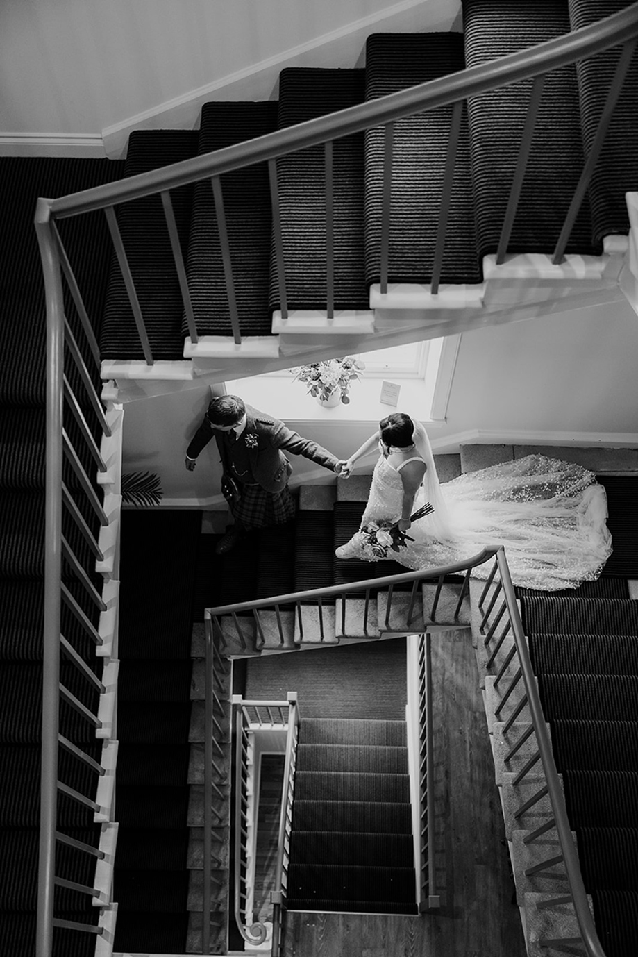 Bride and groom hold hands as they walk down the stairs in House of Elrick. 